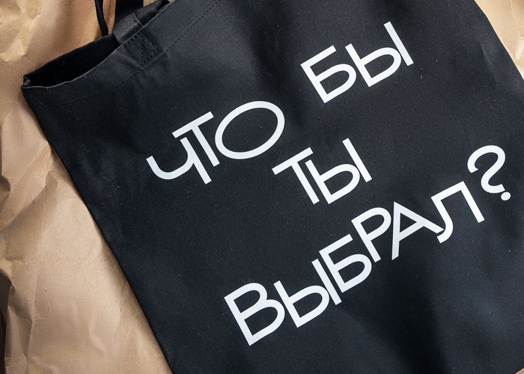 Фотография мерча к юбилейной выставке Динары Асановой: сумка-шоппер чёрного цвета с надписью «Что бы ты выбрал?».