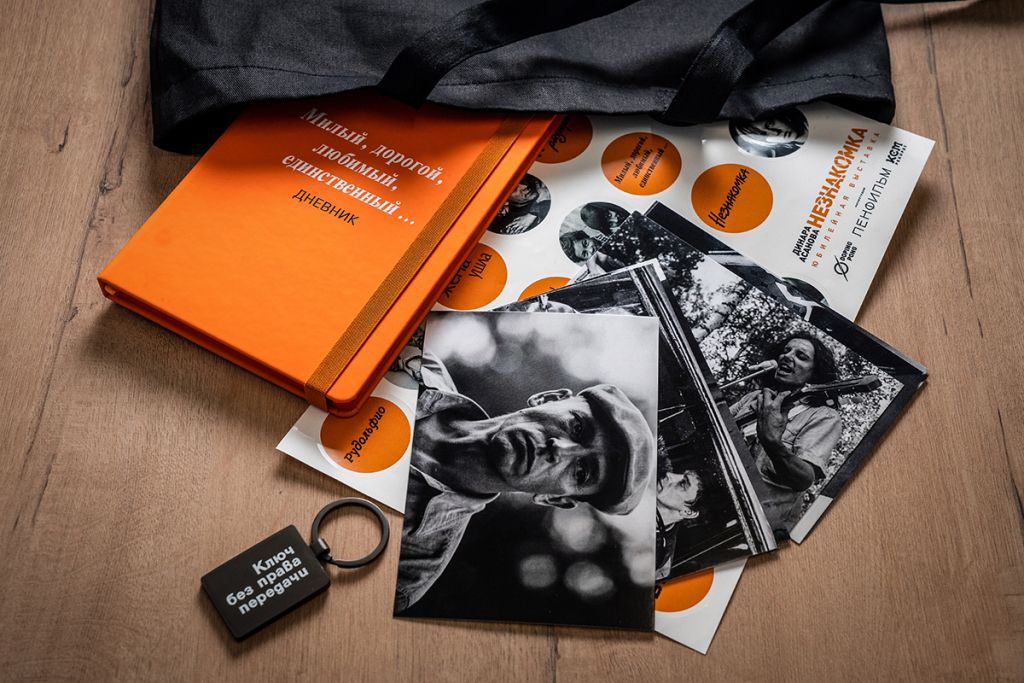 Фотография официального мерча к юбилейной выставке Динары Асановой: сумка-шоппер, дневник, брелок, стикерпак и комплект открыток.
